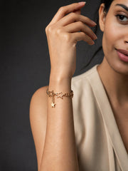 A woman wearing a delicate gold chain bracelet with star charms, shown in a close-up lifestyle shot against a dark gray background.