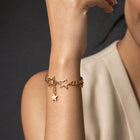 A woman wearing a delicate gold chain bracelet with star charms, shown in a close-up lifestyle shot against a dark gray background.