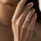 A close-up of a woman's hand wearing a delicate silver ring with a small clear gemstone, set against a soft beige background.