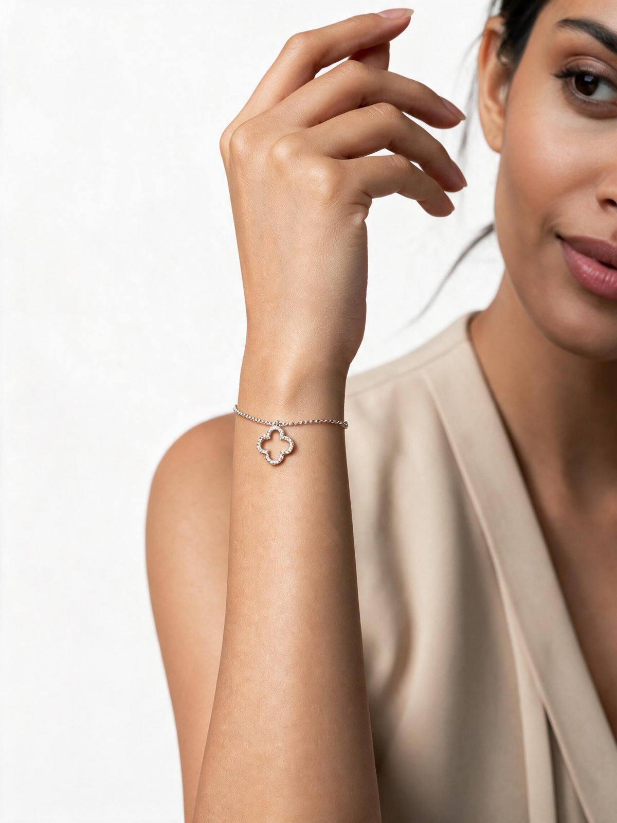 A woman wearing a delicate silver chain bracelet with a small openwork clover or flower charm, shown against a clean light background.