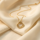 A gold necklace with a double-ring geometric pendant, elegantly draped on soft cream-colored satin fabric.