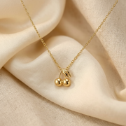 A delicate gold chain necklace with a cherry pendant, displayed on draped cream-colored fabric.