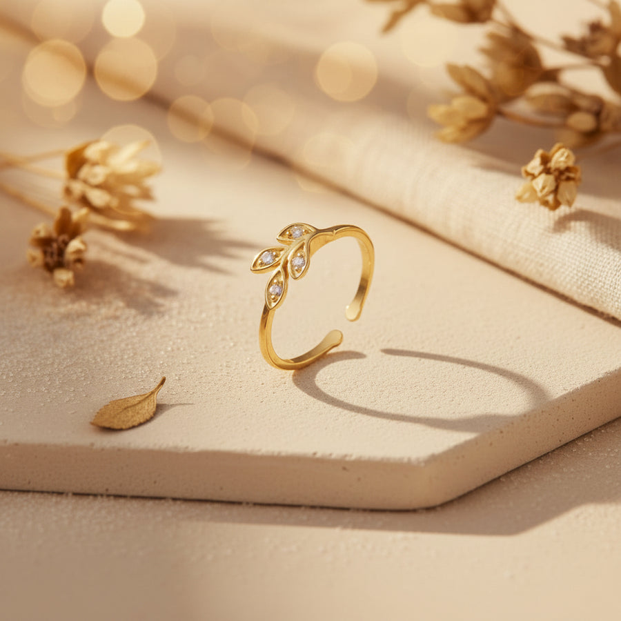 A gold adjustable ring featuring a leafy branch design set with small clear stones, shown on a clean white background with a soft reflection.
