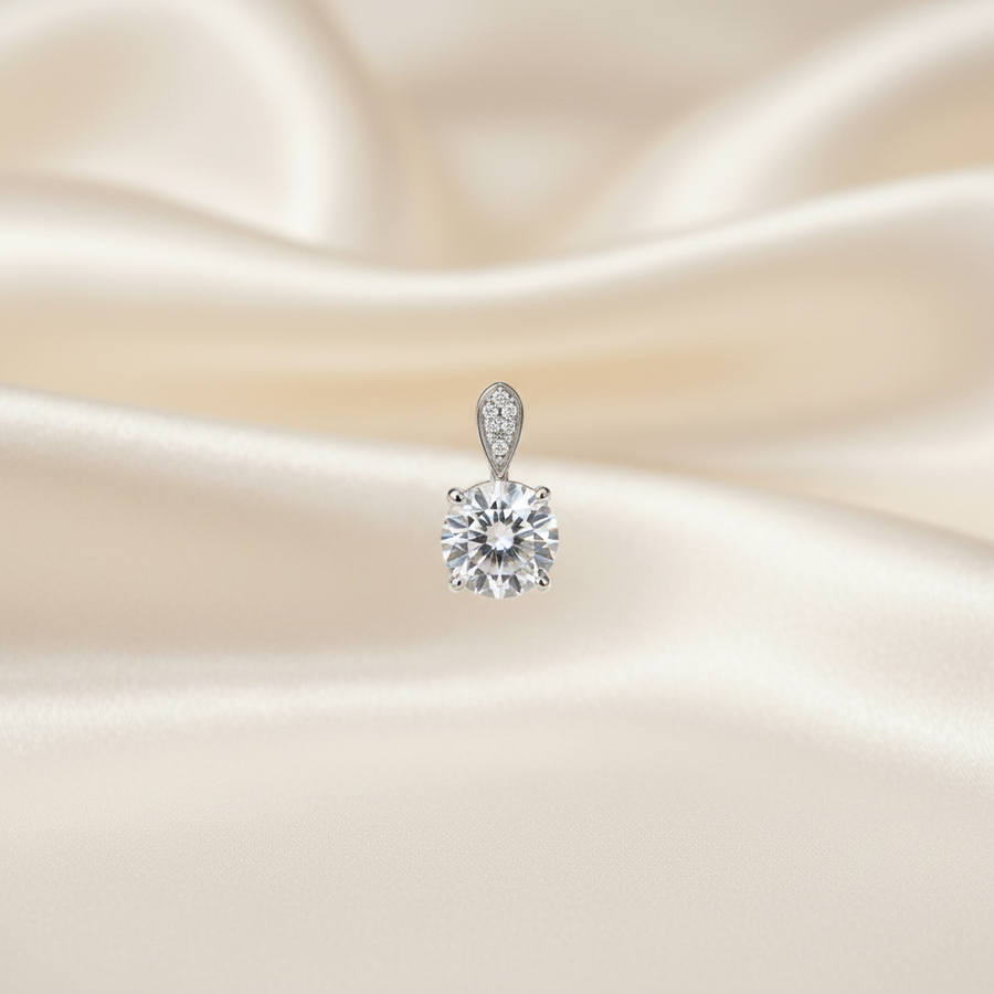 A single solitaire diamond pendant in a silver setting, centered against a draped cream satin fabric background.