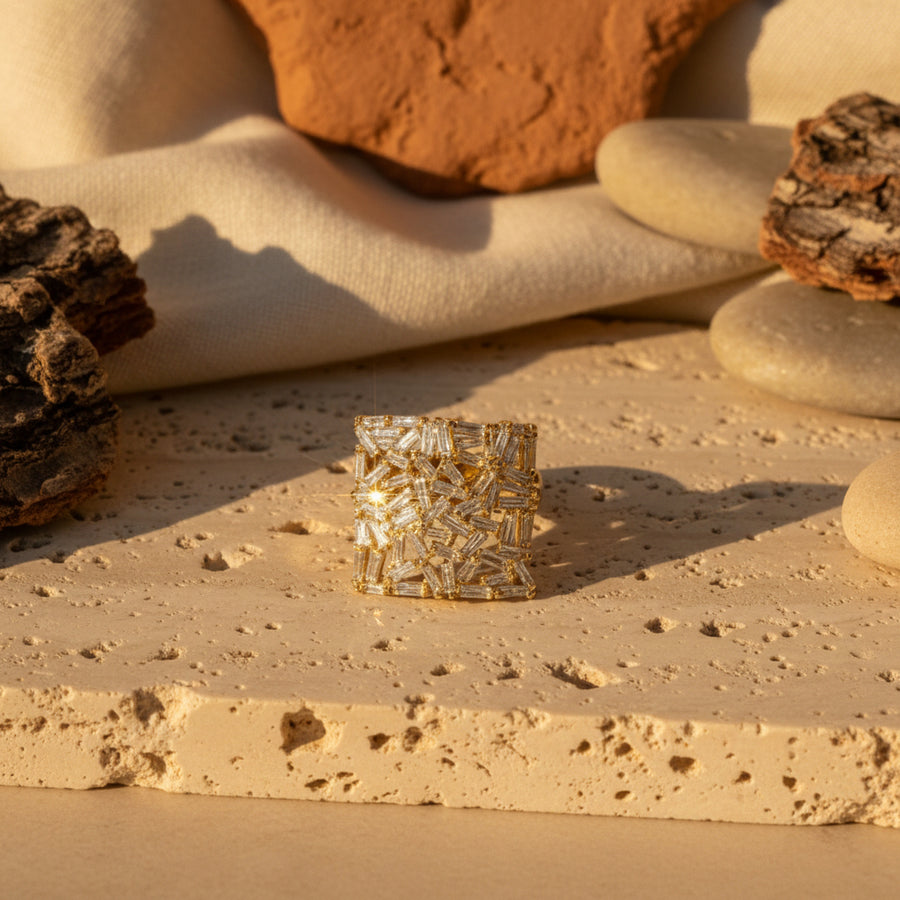 A close-up lifestyle shot of a model wearing a large, square gold ring adorned with intricate white floral or leaf-like inlay patterns.