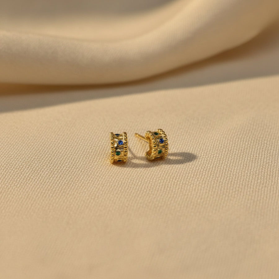A pair of small gold-toned stud earrings displayed on a white textured foam insert inside a white jewelry box.